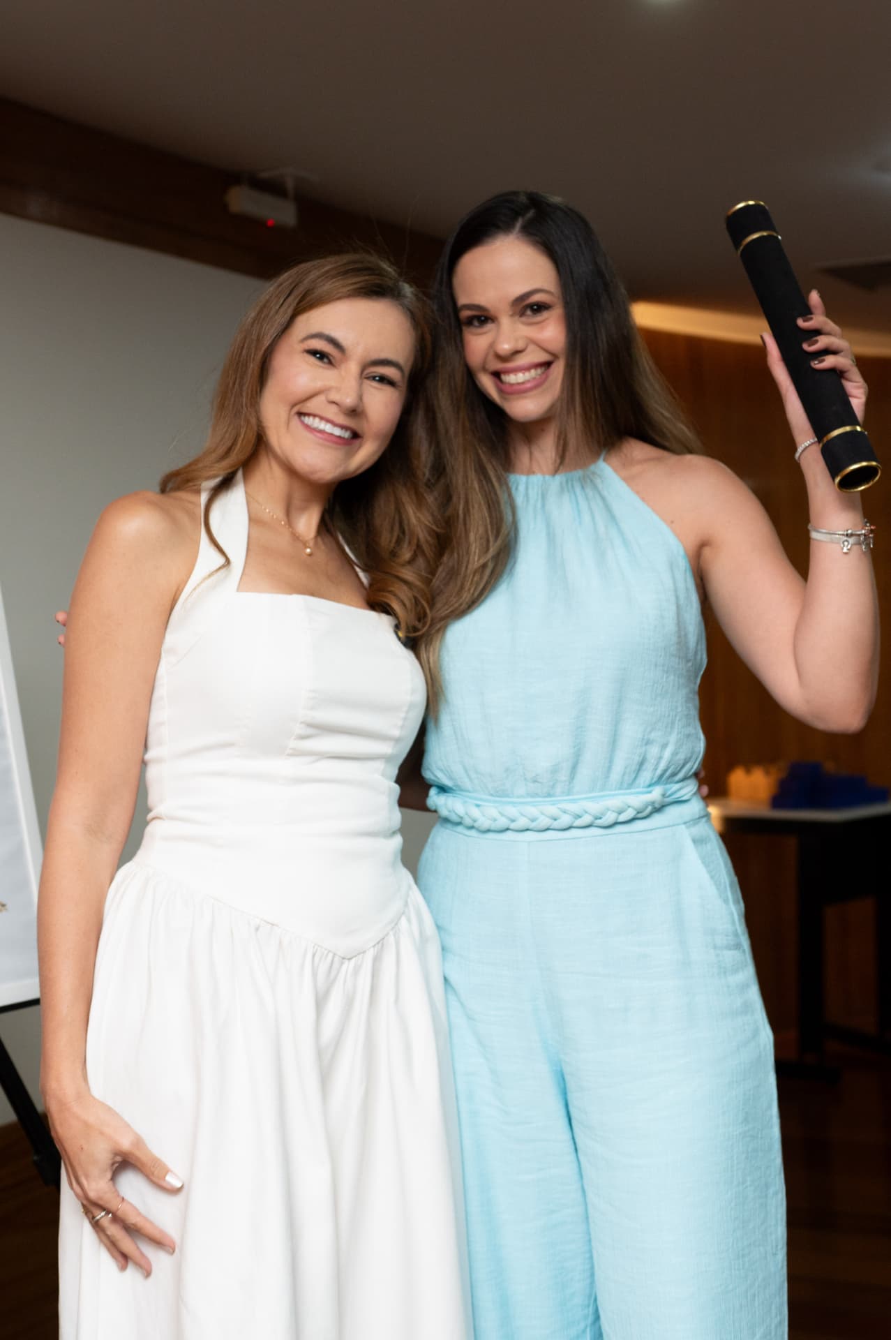 2ª turma — formanda erguendo o canudo de formatura ao lado da professora