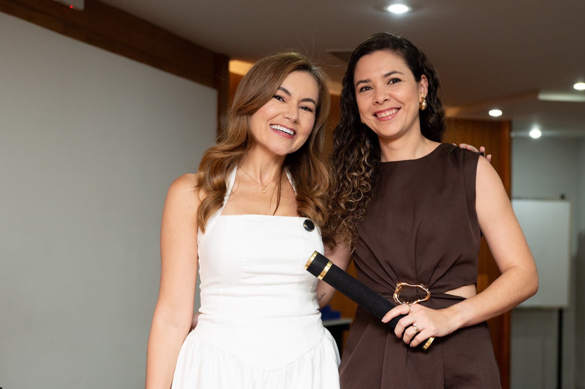 2ª turma — duas formandas abraçadas, uma de branco e outra de vestido marrom com o canudo